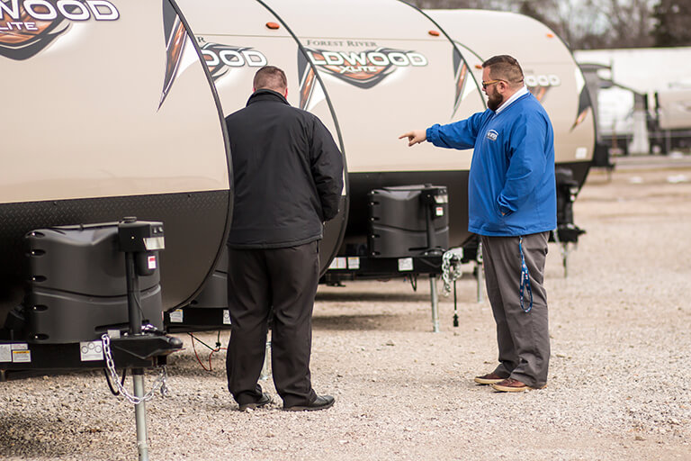 All American Coach / RV Wholesale Superstore employee shows customer a travel trailer on the lot.